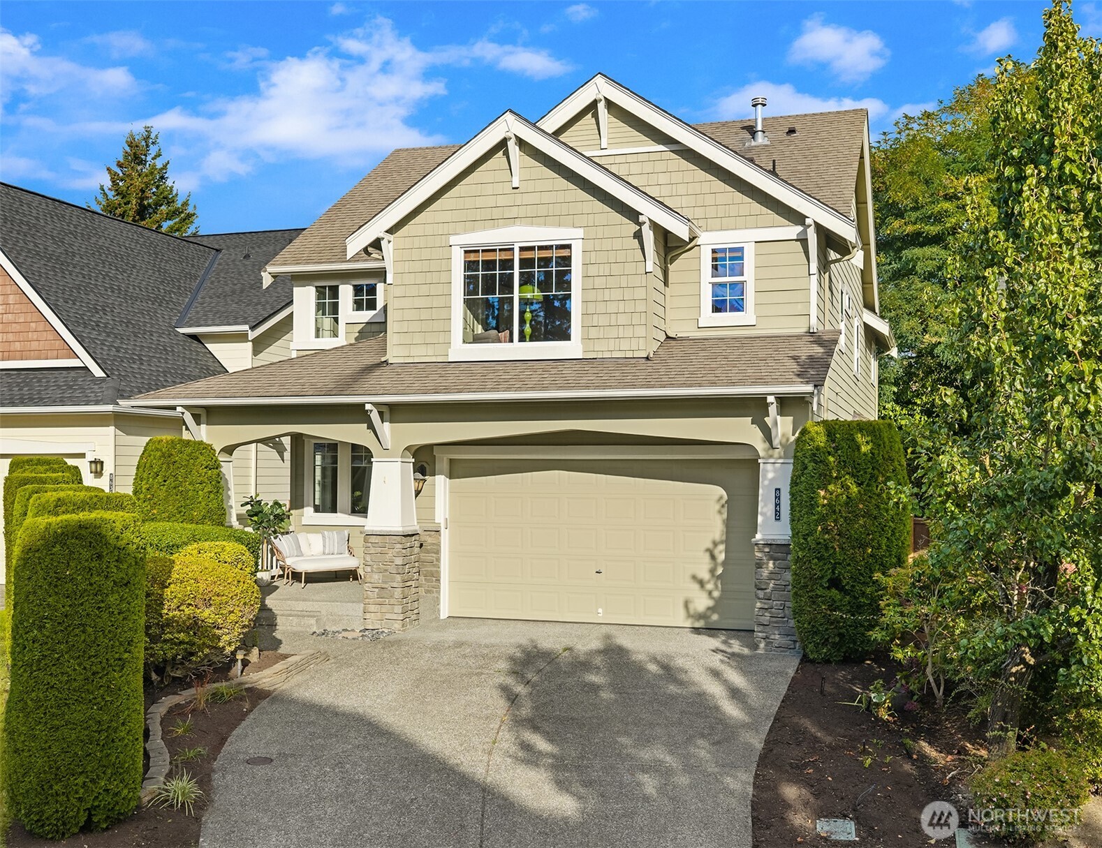 Sage-green two-story home with a double garage, stone porch columns, and manicured hedges.