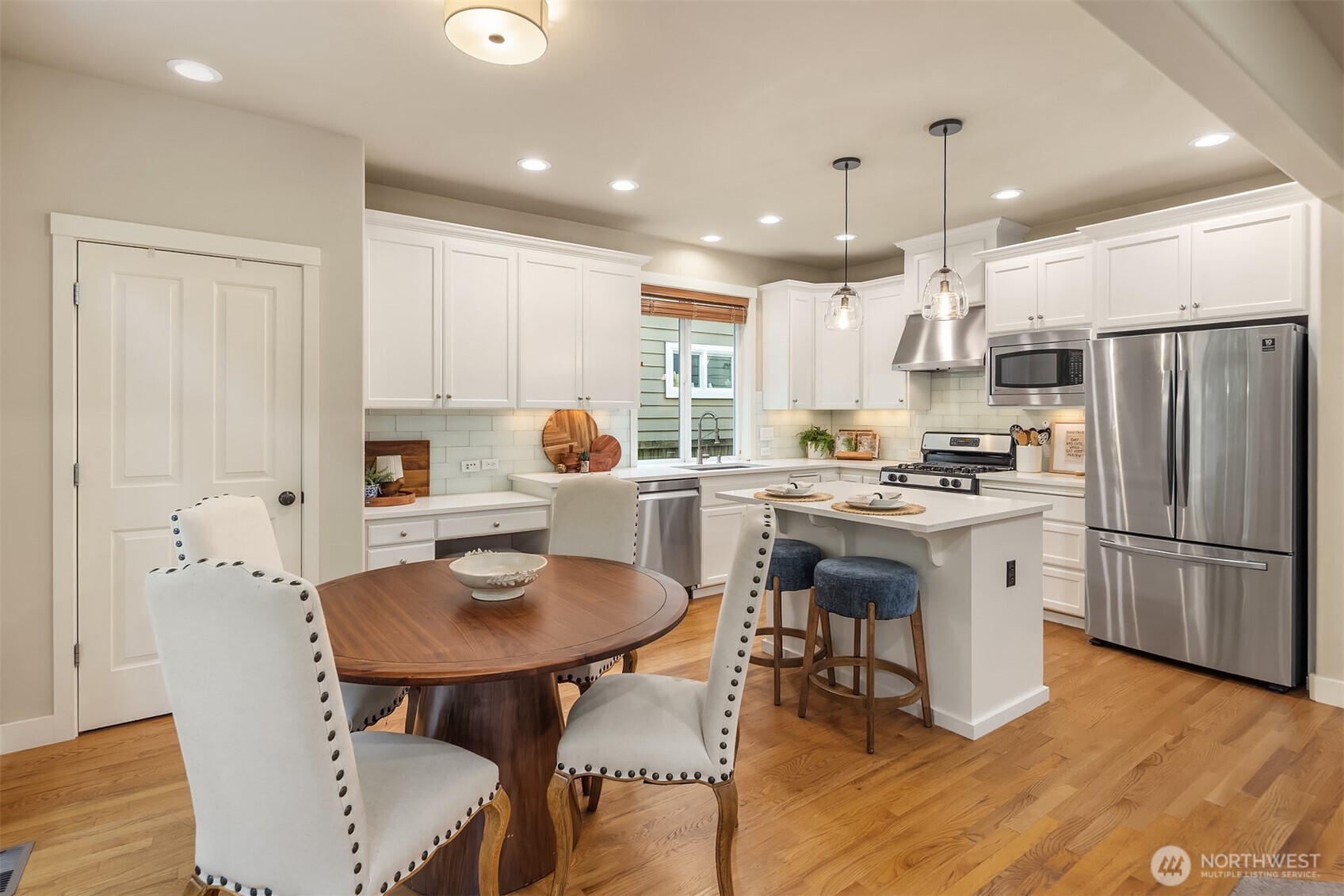Bright kitchen with white cabinets, stainless steel appliances, a central island, and adjoining dining table.