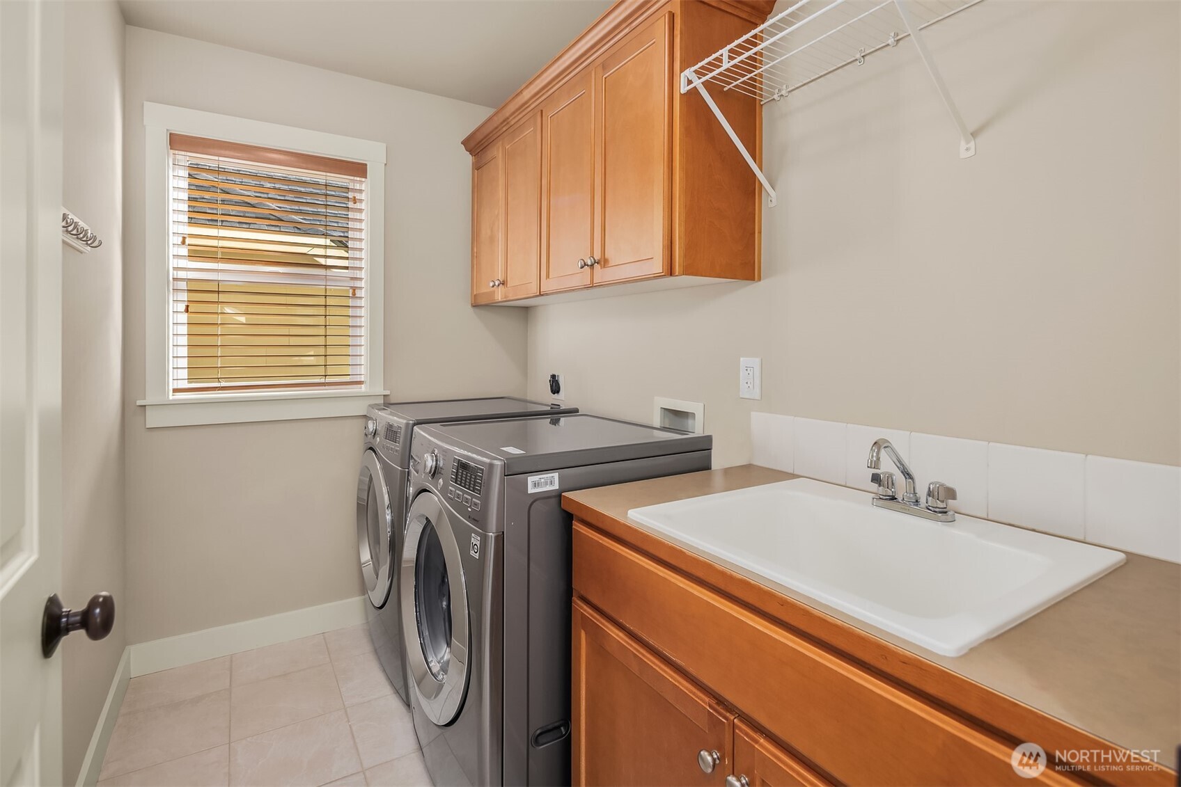 Laundry room with front-loading washer and dryer, utility sink, and warm wood cabinetry.