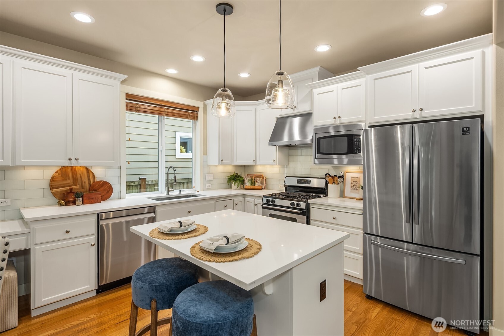 White kitchen with a large island, stainless steel appliances, and two blue stools.