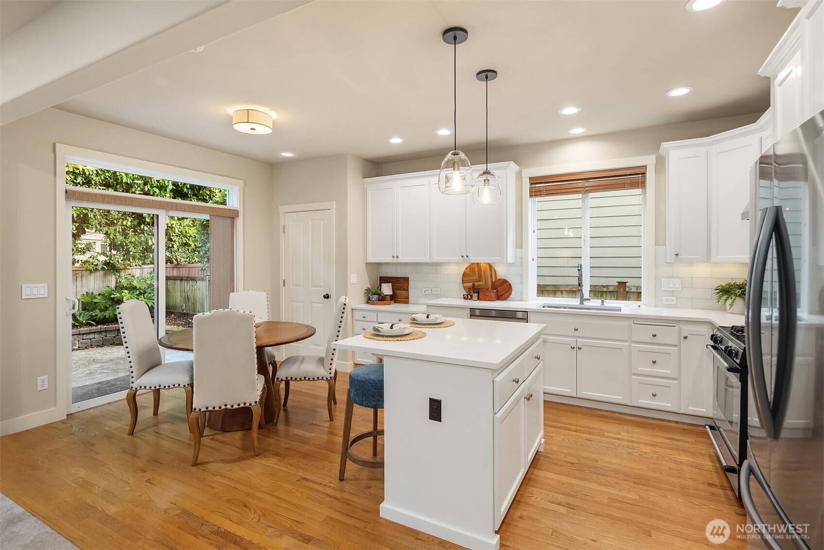 Kitchen with a large white island, shaker cabinets, hardwood floors, and an adjoining dining area.