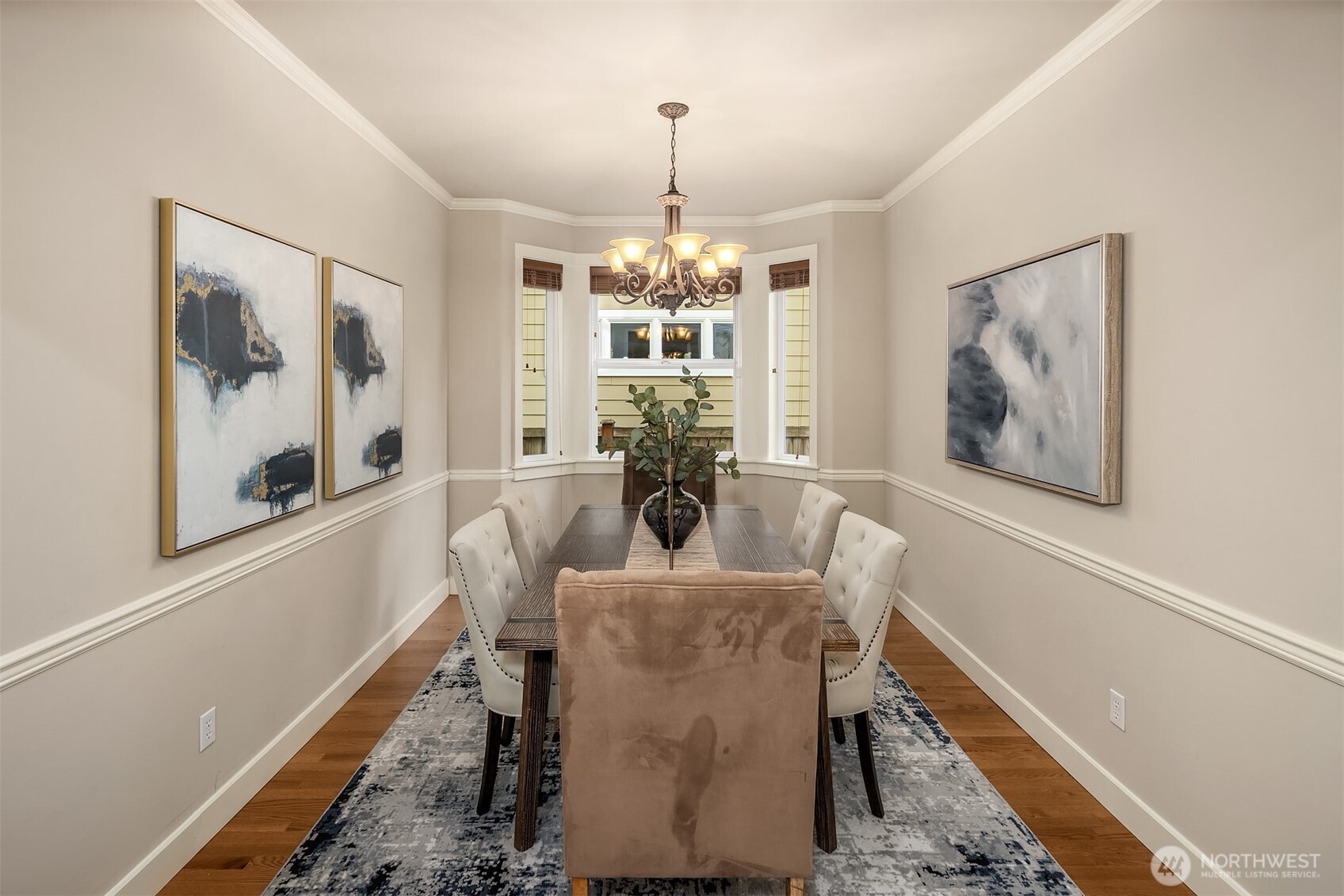 Dining room with a dark wood table, upholstered chairs, and a chandelier beneath a bay window.