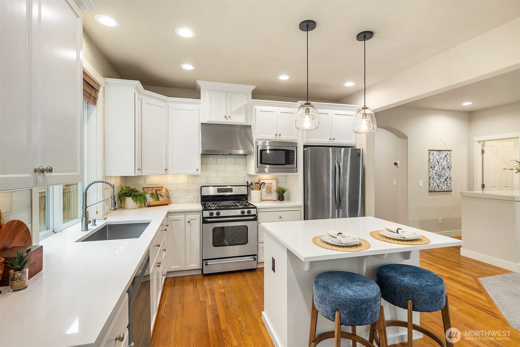White kitchen with stainless steel appliances, a large island, and blue upholstered stools.