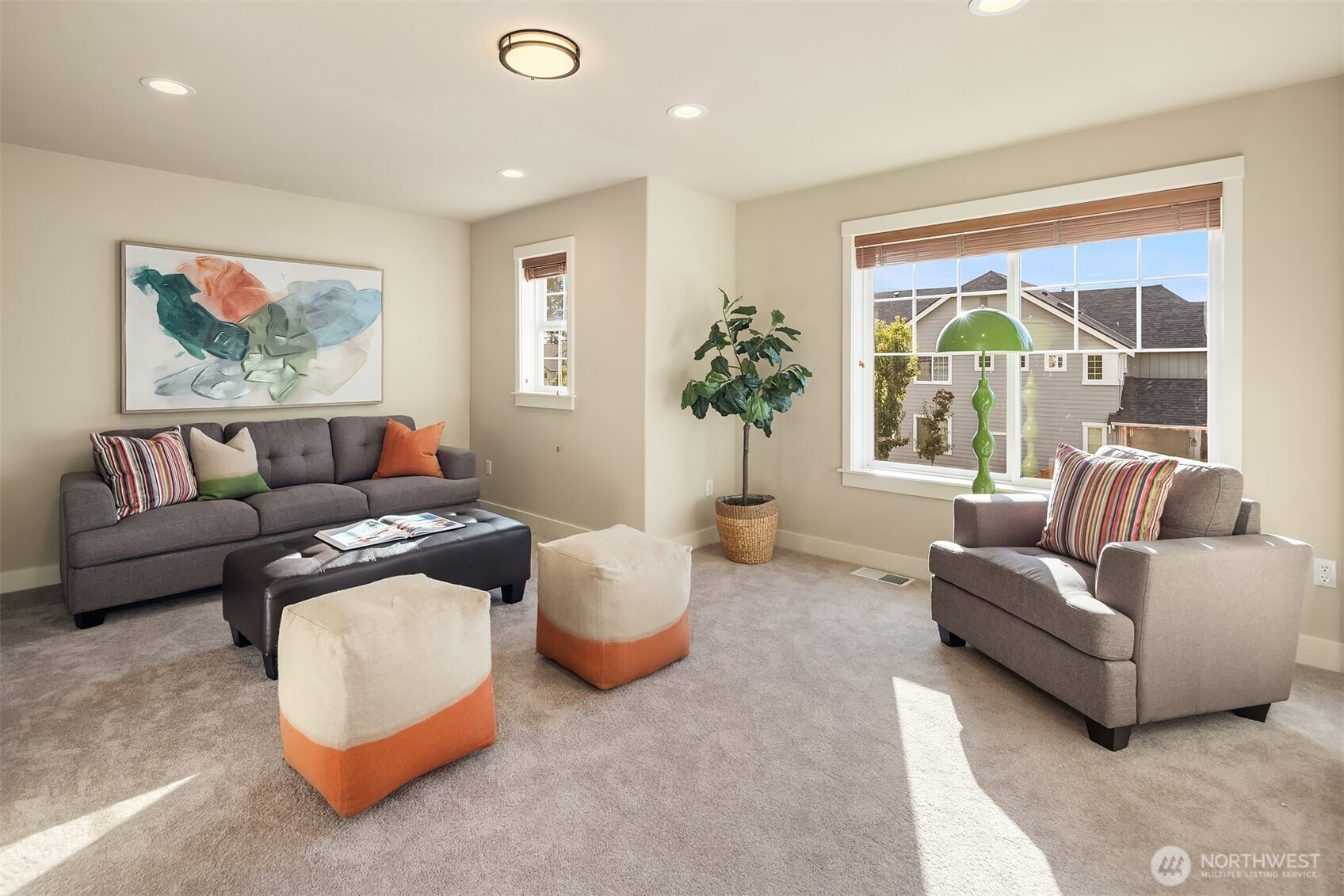 Staged living room with gray seating, orange-accented ottomans, and a large sunlit window.