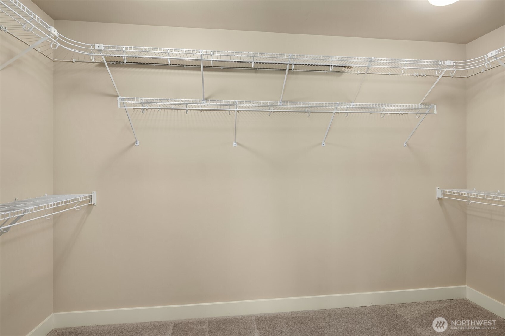 Empty walk-in closet with white wire shelving and carpeted floor.