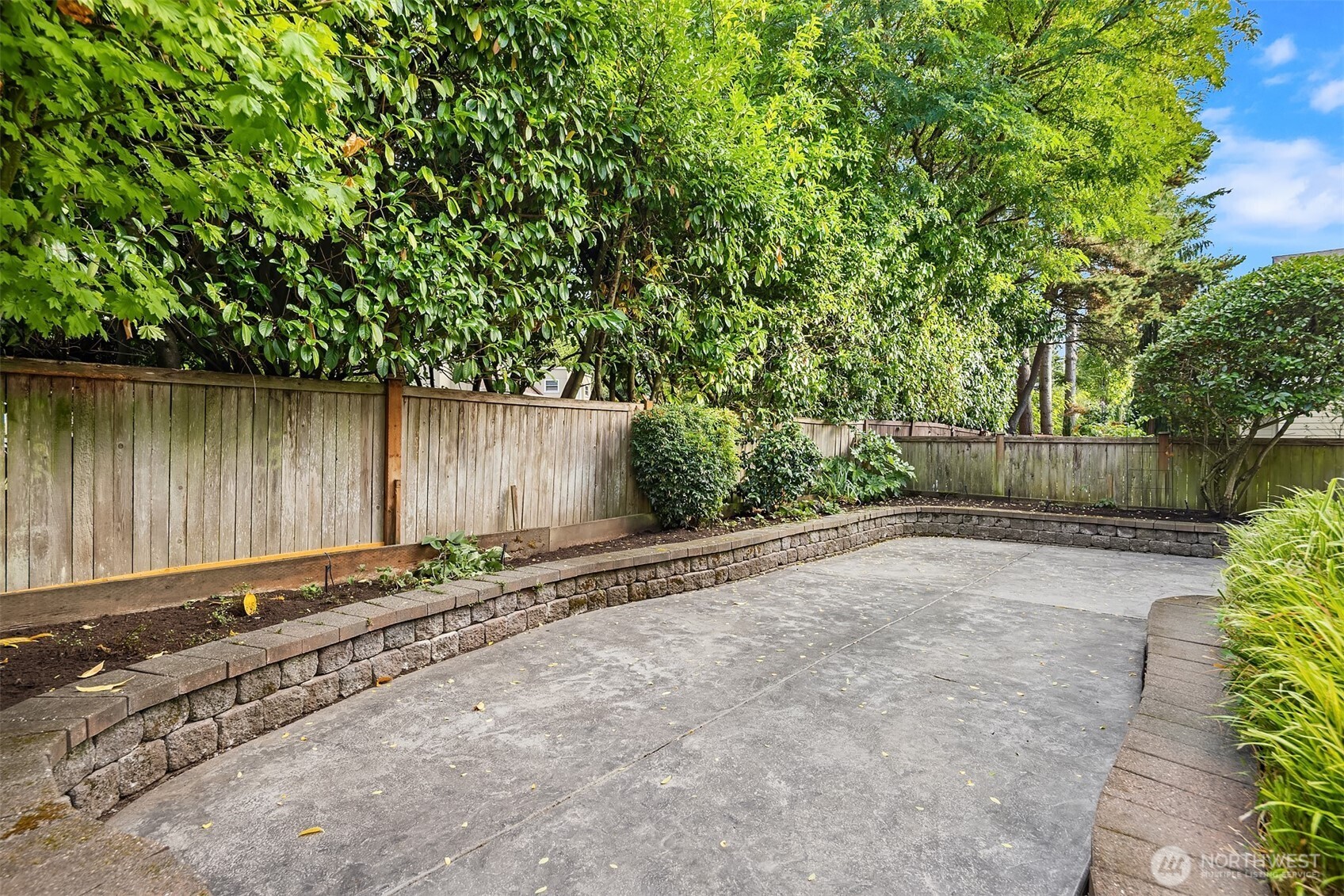 Concrete patio with raised stone planters, a wooden privacy fence, and dense greenery.