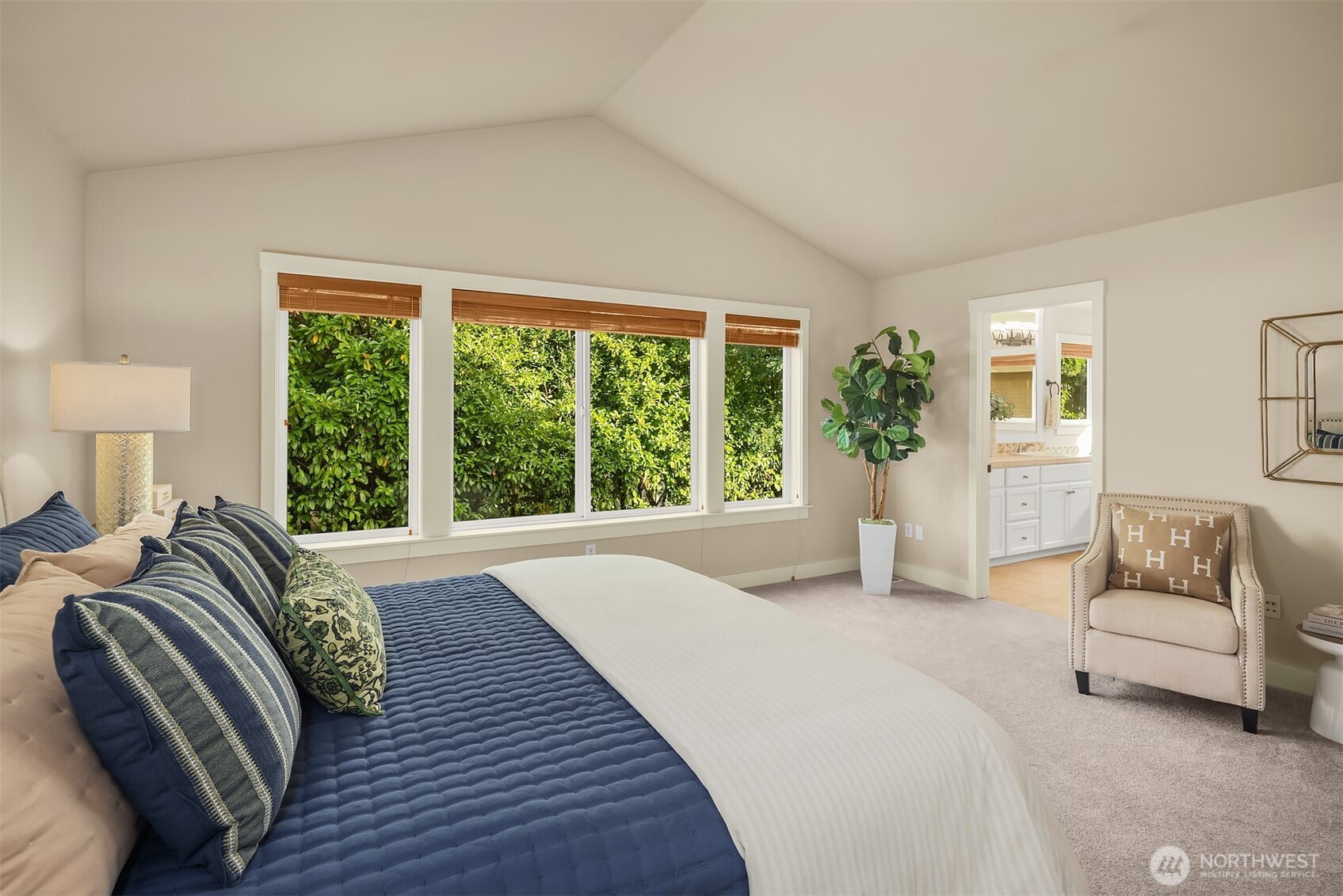 Staged bedroom with vaulted ceiling, navy bedding, and wide windows overlooking greenery.