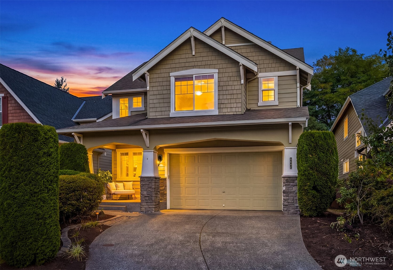 Two-story home with a wide garage and warmly lit windows at dusk.