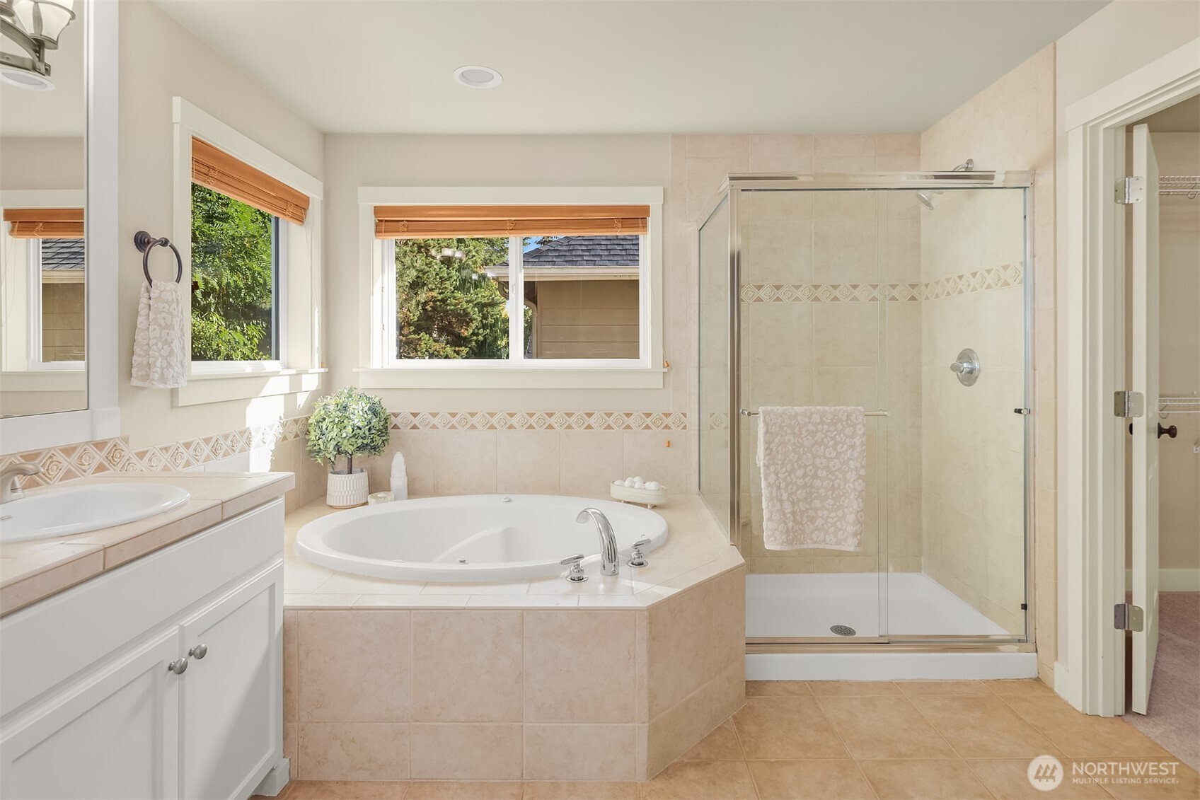 Bathroom with a built-in soaking tub, glass shower, and windows overlooking greenery.