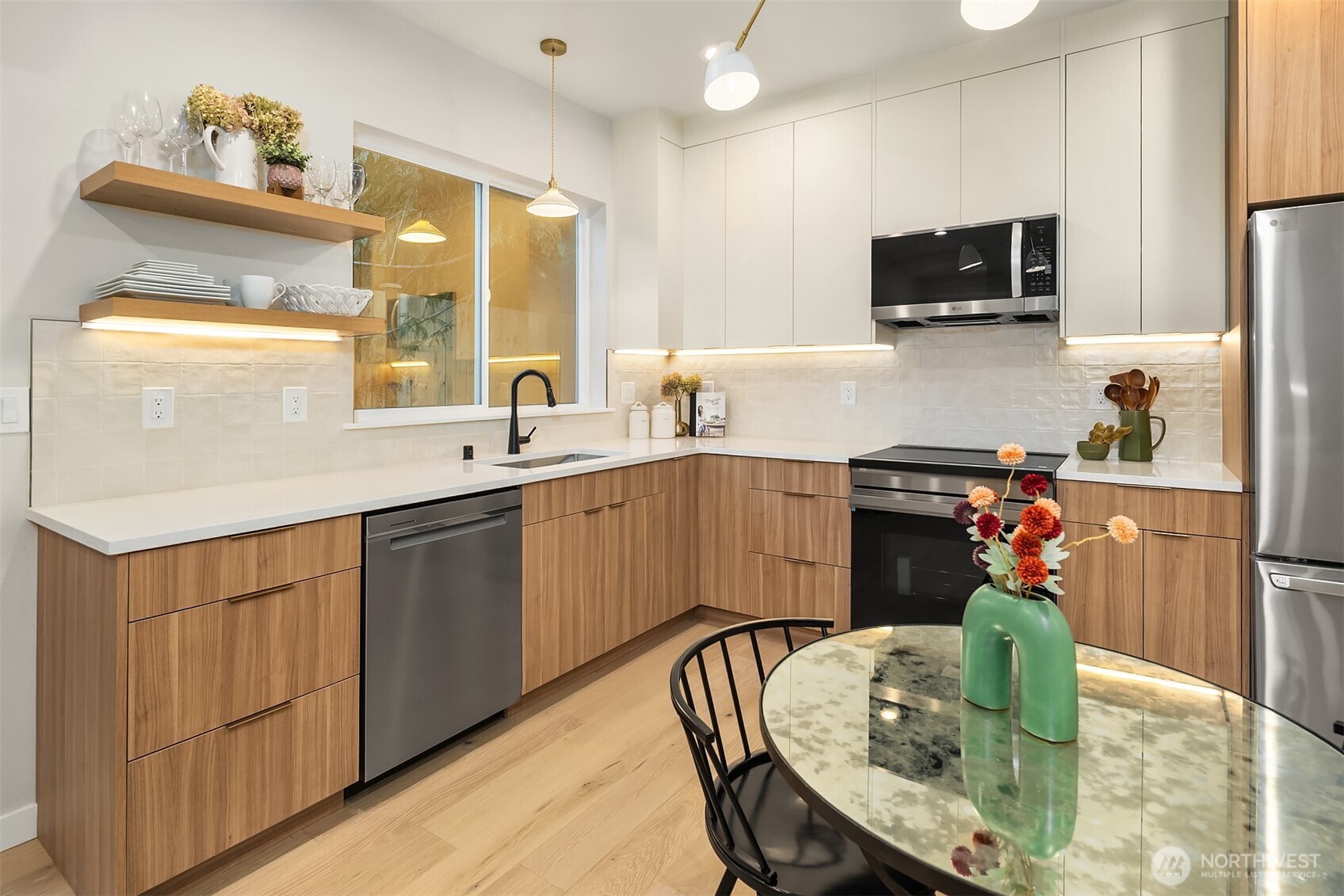 Modern kitchen with warm wood cabinetry, white cabinets, and an oval glass-top dining table.