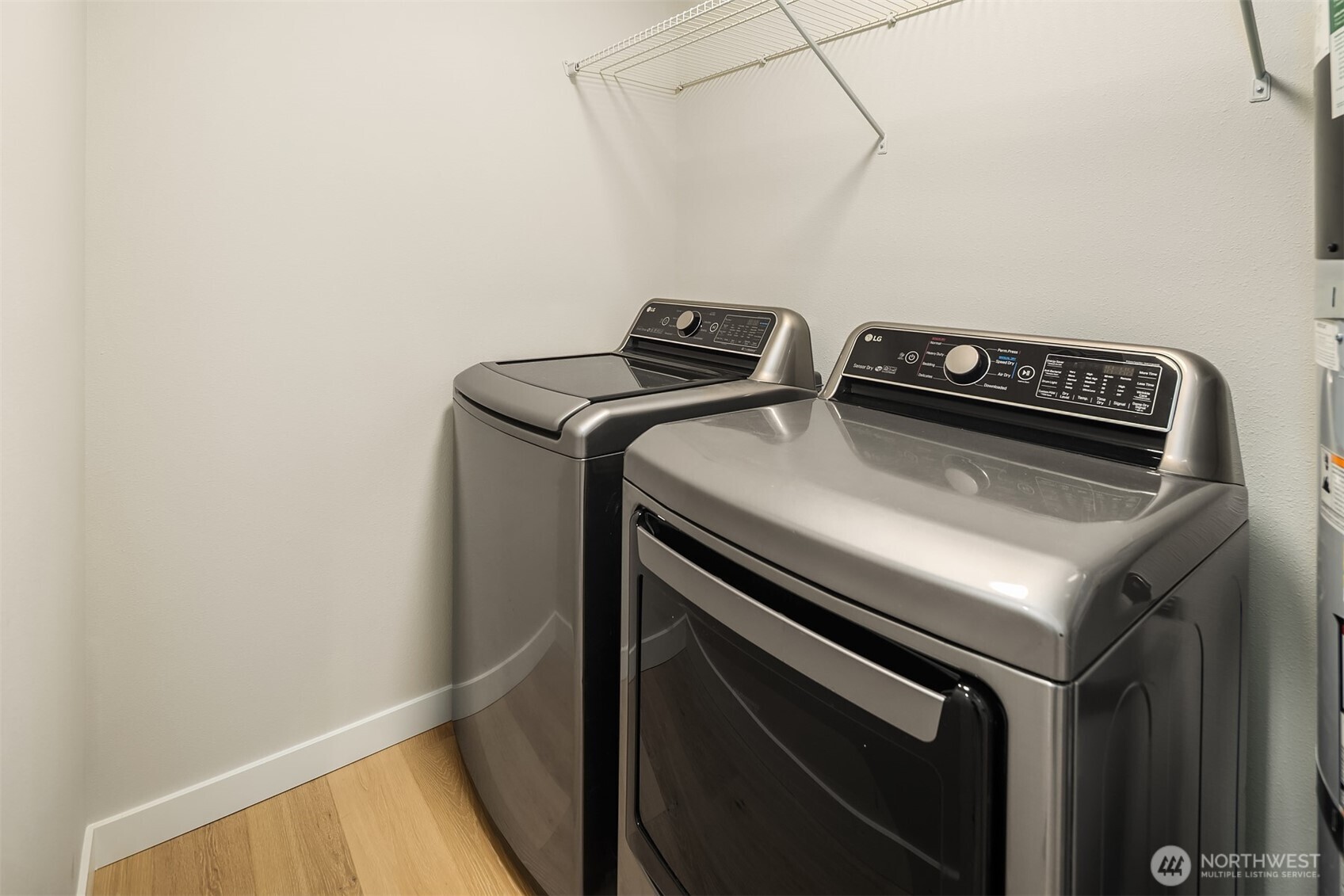 Laundry room with metallic washer and dryer beneath wire shelving.