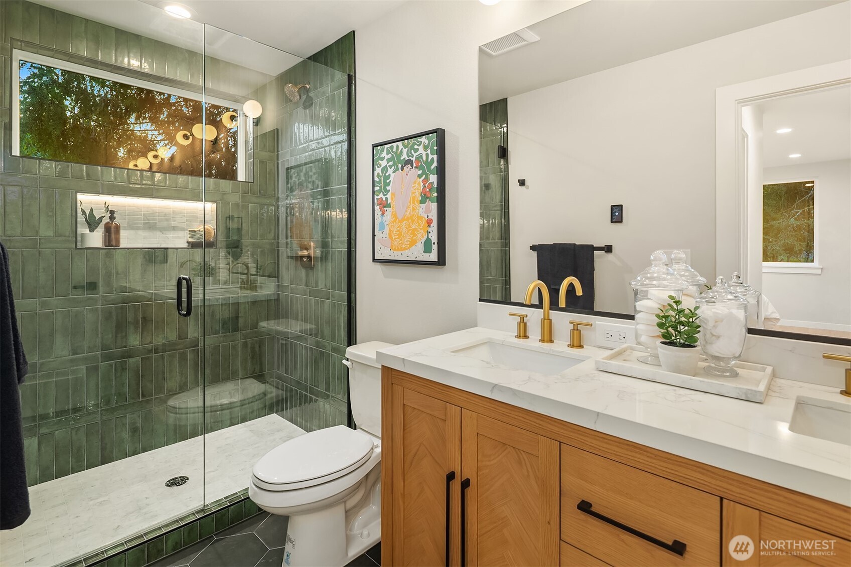 Bathroom with a green-tiled glass shower and wood vanity with brass faucets.