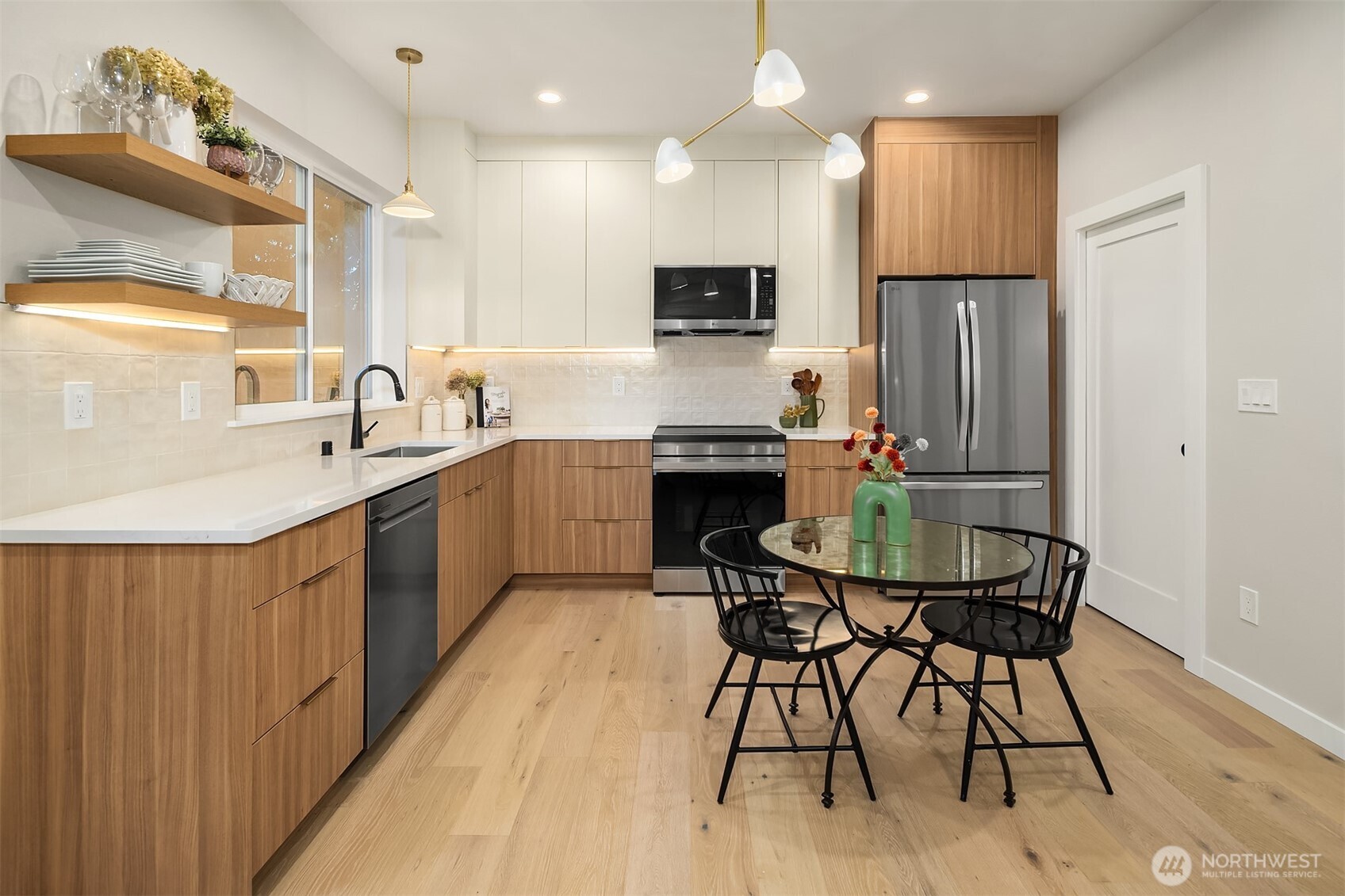 Modern kitchen with warm wood cabinets, stainless steel appliances, and a round glass dining table.