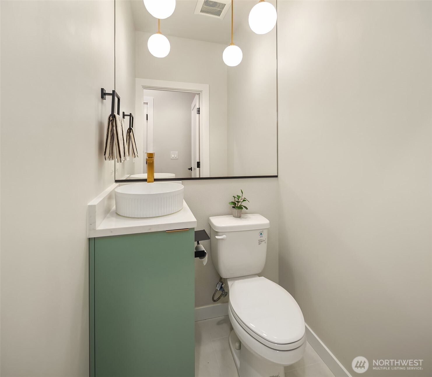 Bathroom with a sage-green vanity, vessel sink, gold faucet, and globe pendant lights.