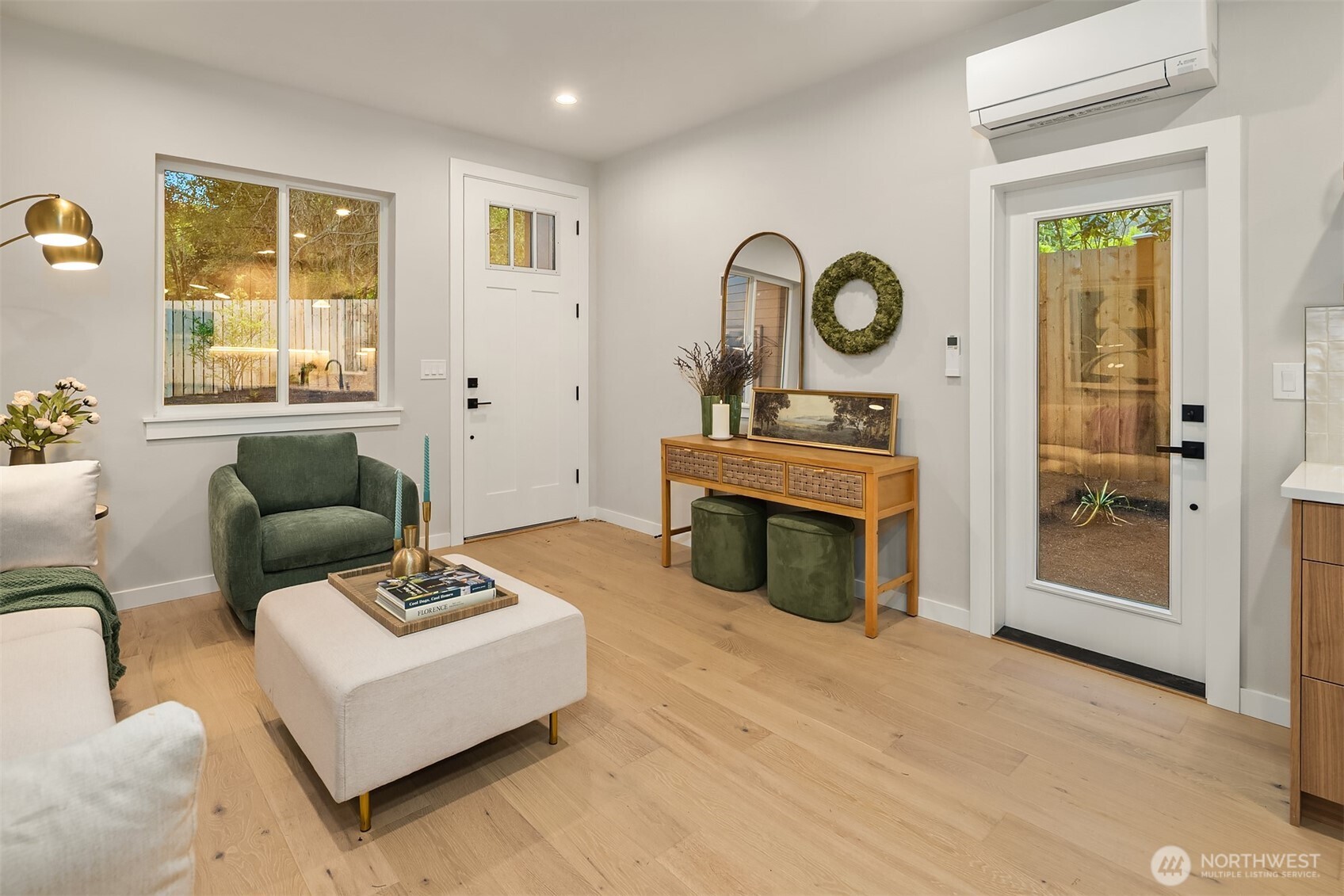 Staged entry and sitting area with a green armchair, oak floors, and a glass door to the fenced yard.