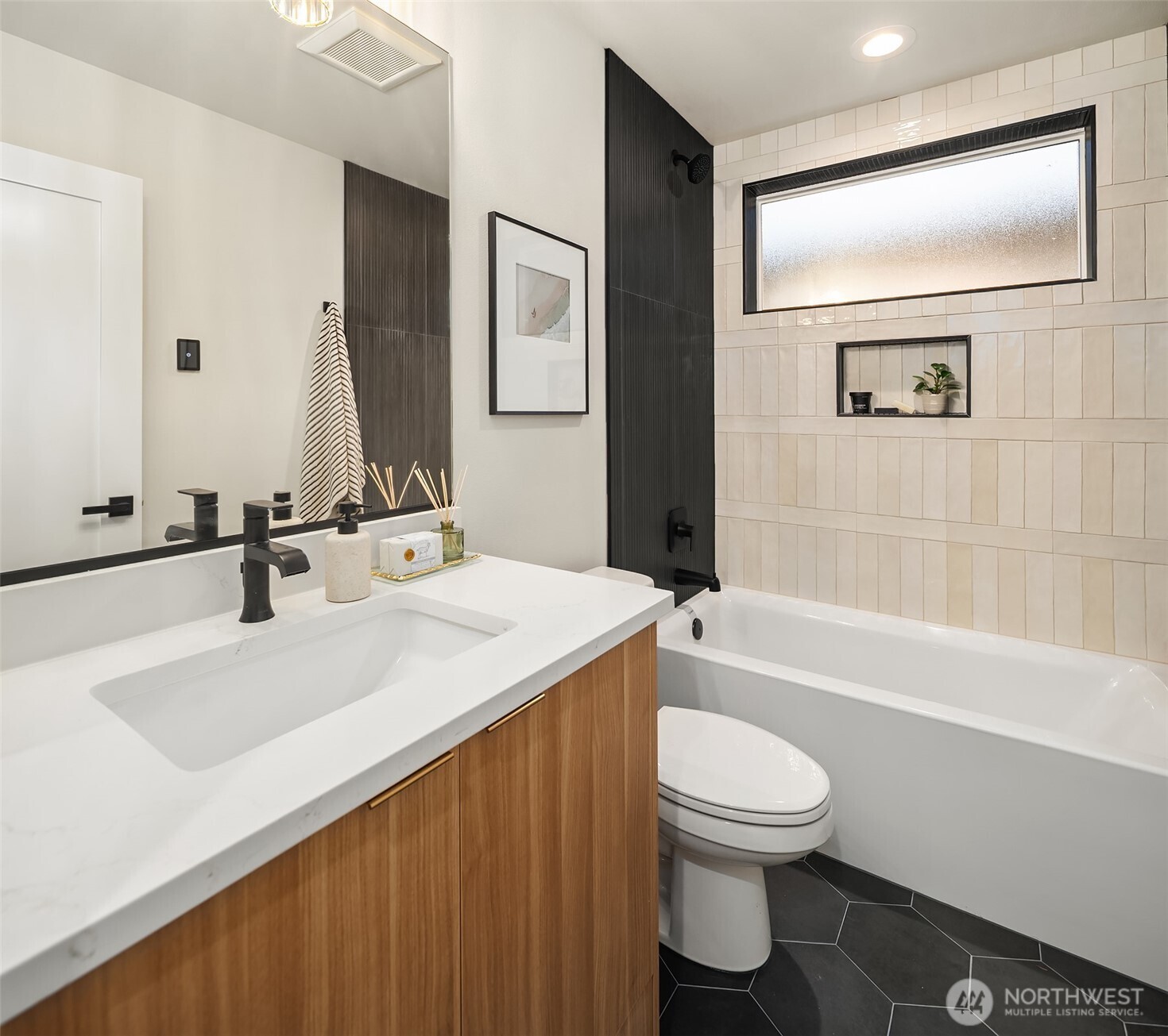 Modern bathroom with a wood-front vanity, cream tub surround, dark tile accent, and frosted window.