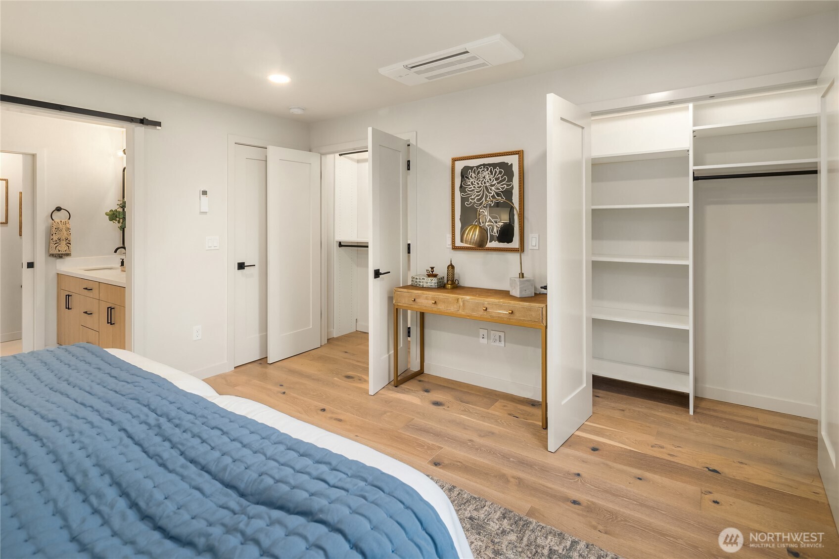 Bedroom with a blue quilted bedspread, open built-in closet, and light oak floors.
