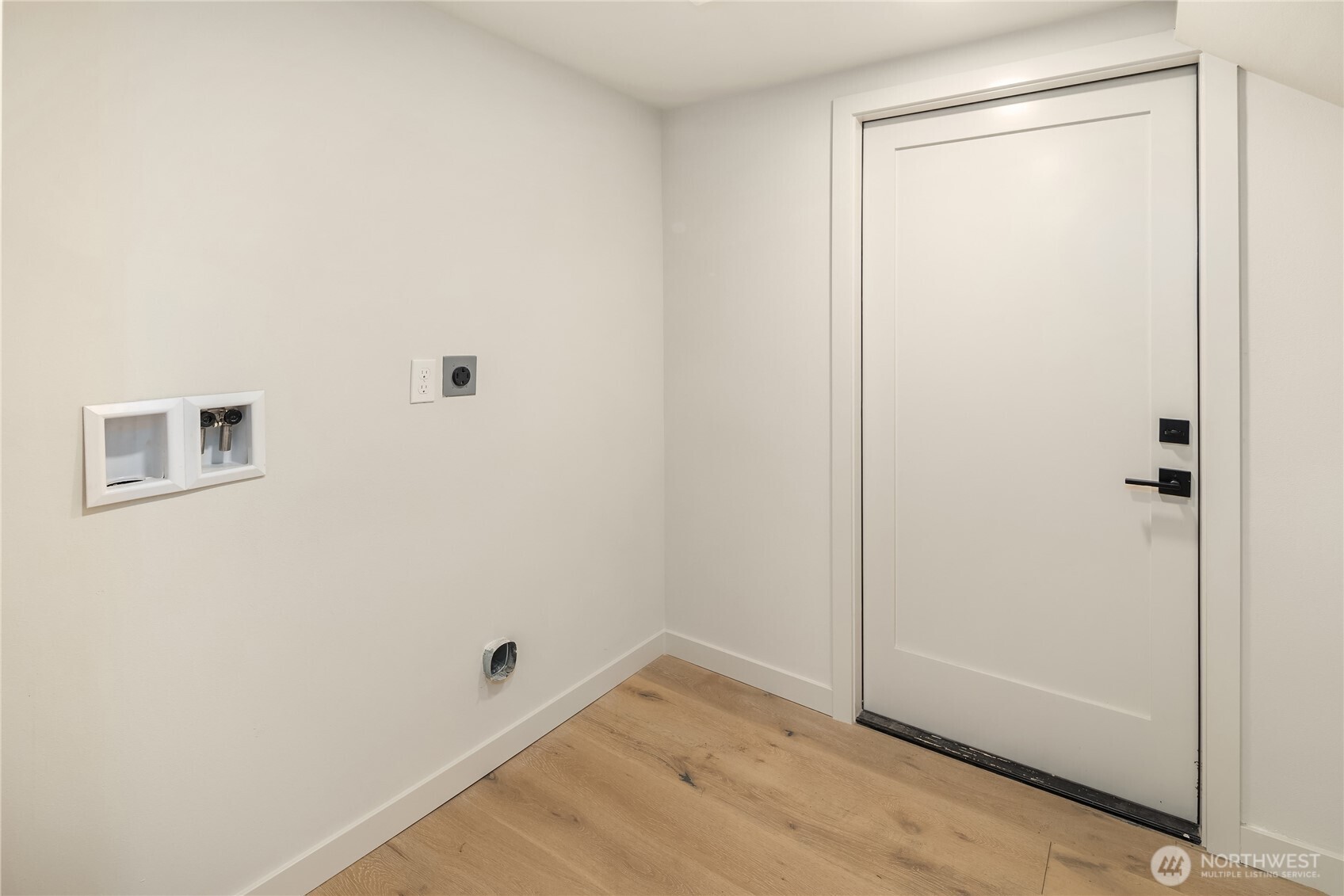 Laundry area with washer hookups, dryer vent, light wood flooring, and a white door.