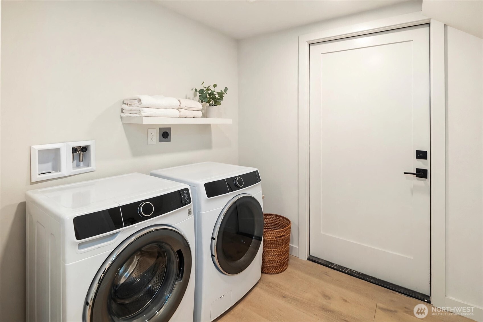 Laundry room with front-loading washer and dryer, folded towels on a shelf, and a woven basket.