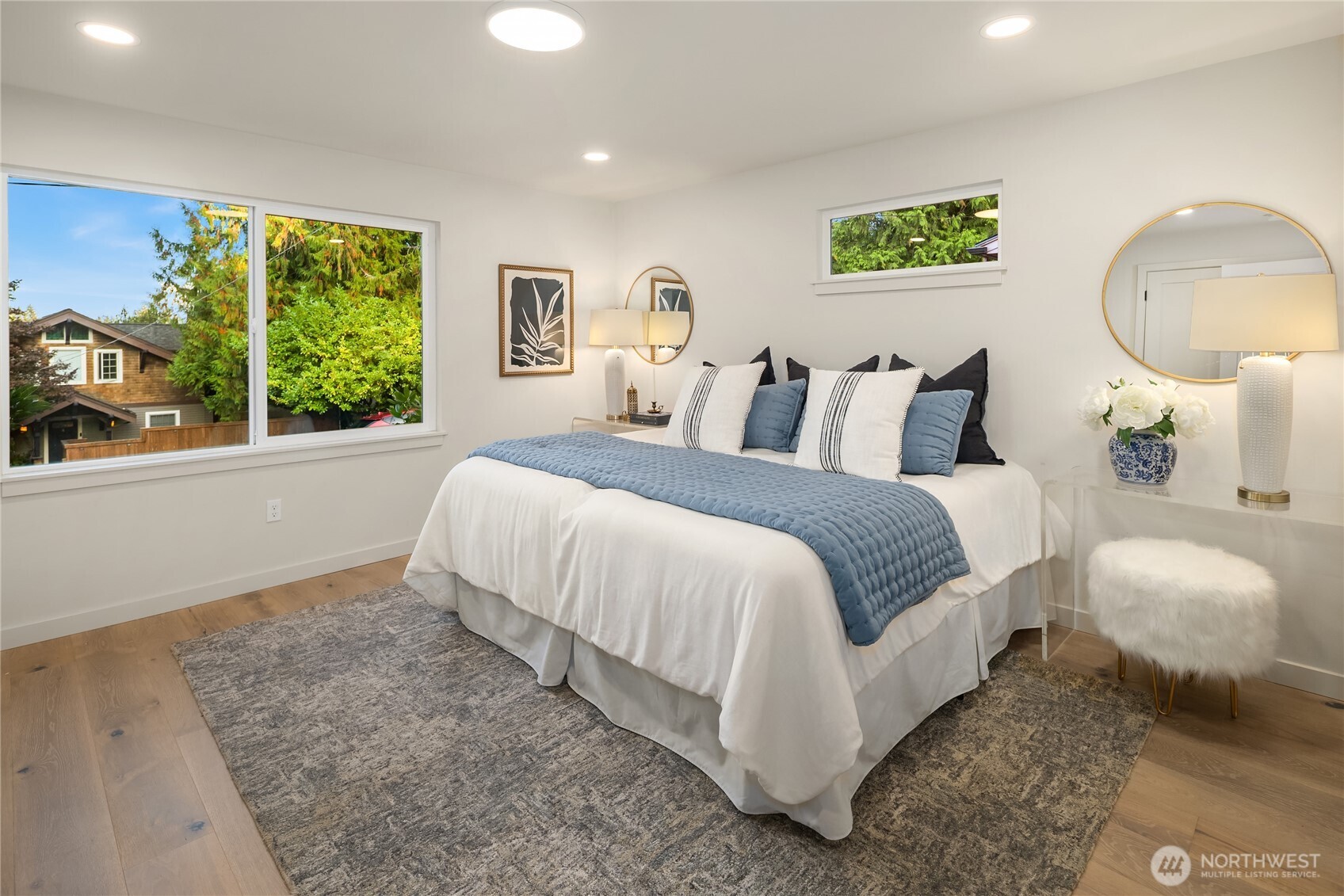 Staged bedroom with blue-and-white bedding, wood floors, and large windows overlooking trees.