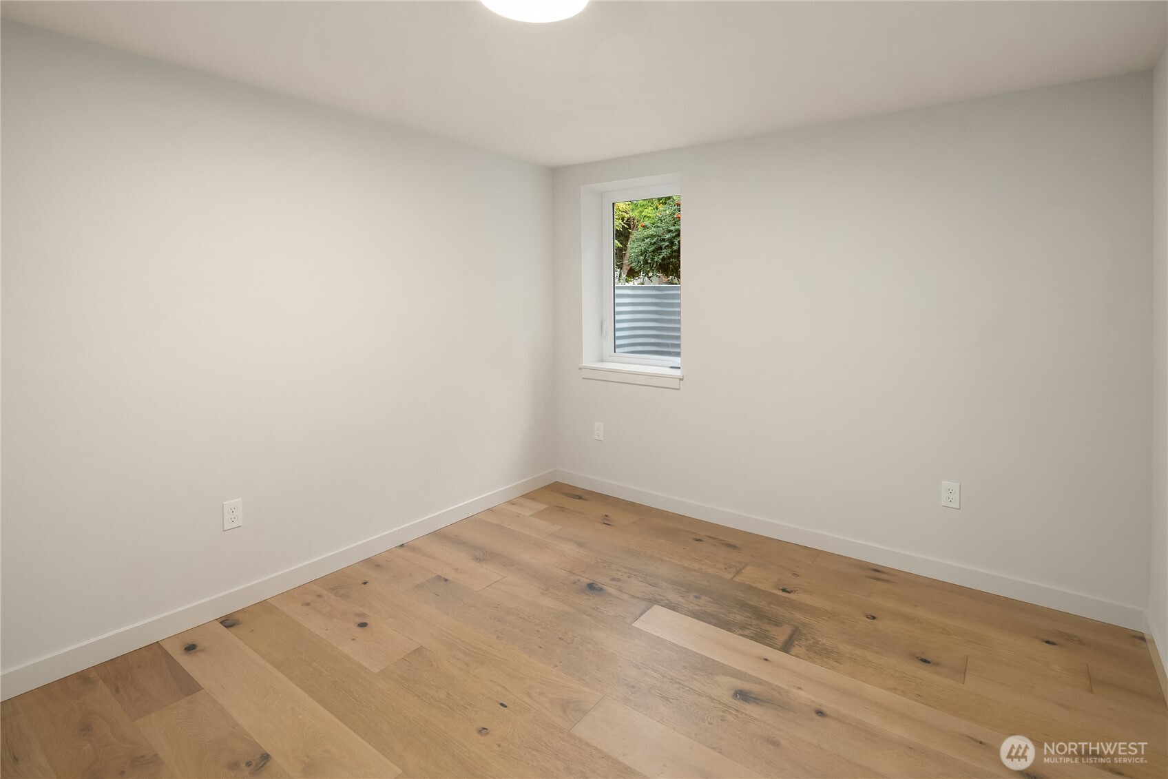 Empty room with light hardwood floors, white walls, and a narrow window.