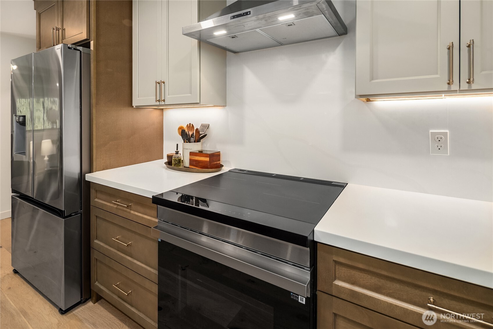 Kitchen with white countertops, warm brown cabinets, stainless-steel refrigerator, and black range.