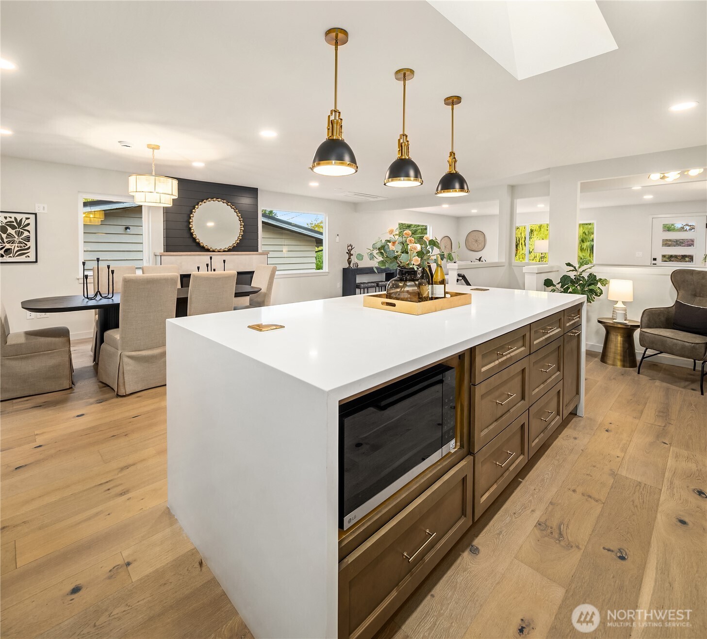 Open-plan kitchen with a white waterfall island, wood cabinetry, and three pendant lights.