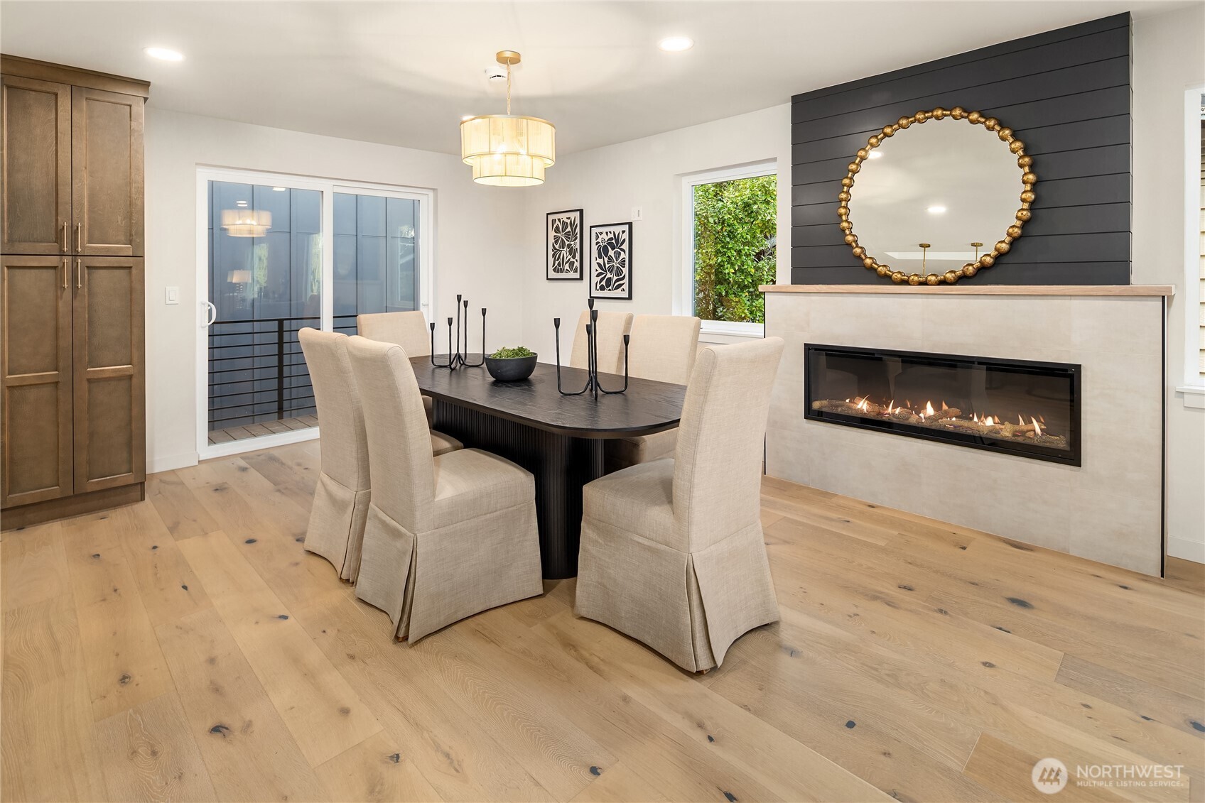 Staged dining room with a linear fireplace, black accent wall, and wide-plank wood floors.