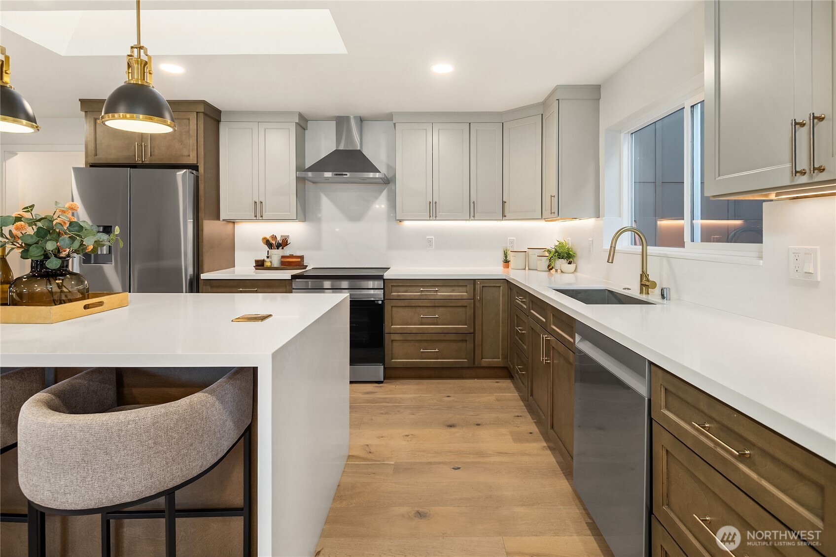 Kitchen with a white island, two-tone cabinets, stainless steel appliances, and a sink beneath a window.