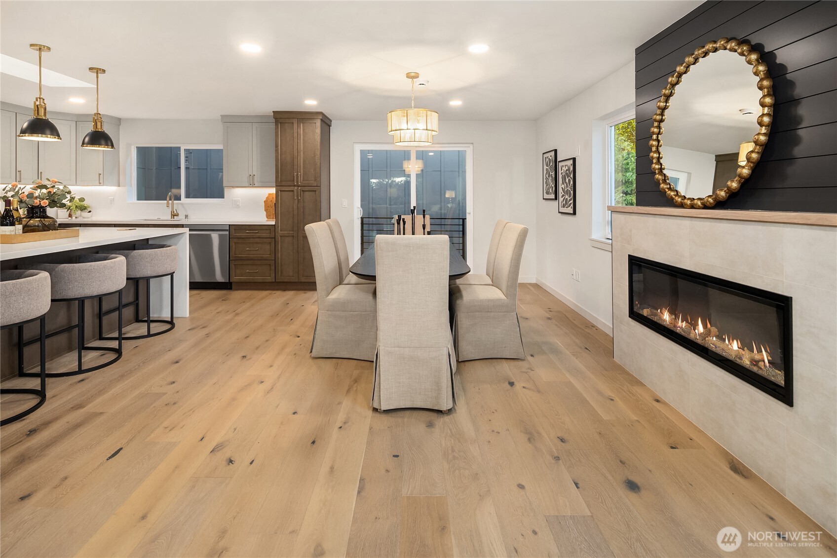 Open kitchen and dining area with oak floors, island seating, and a modern fireplace.