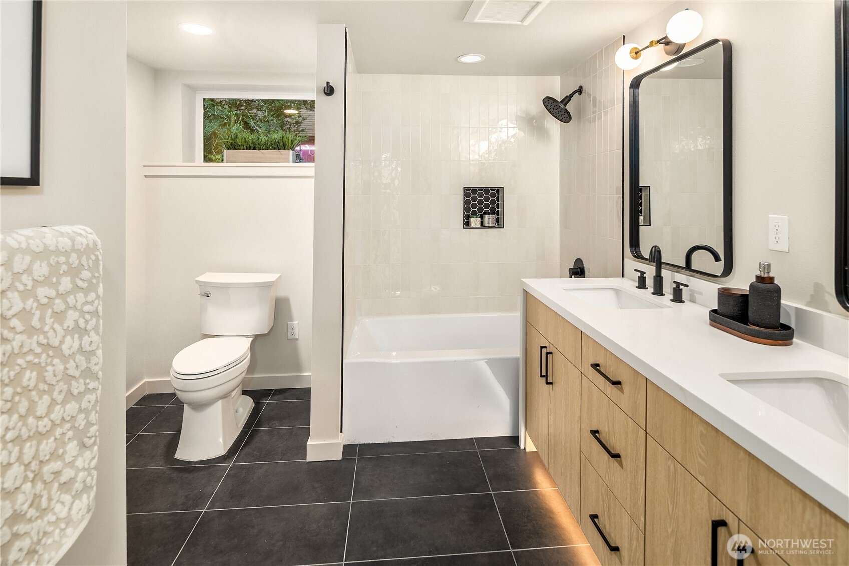 Renovated bathroom with a tiled tub and shower, black fixtures, and a light wood double vanity.
