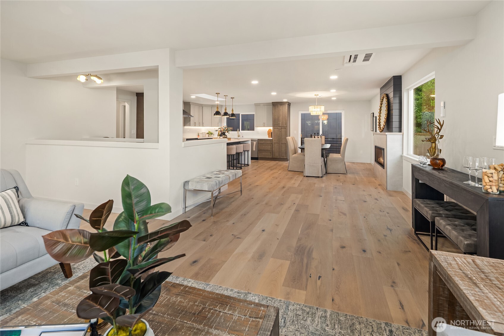 Open-plan living, dining, and kitchen area with light wood floors, an island, and a fireplace.