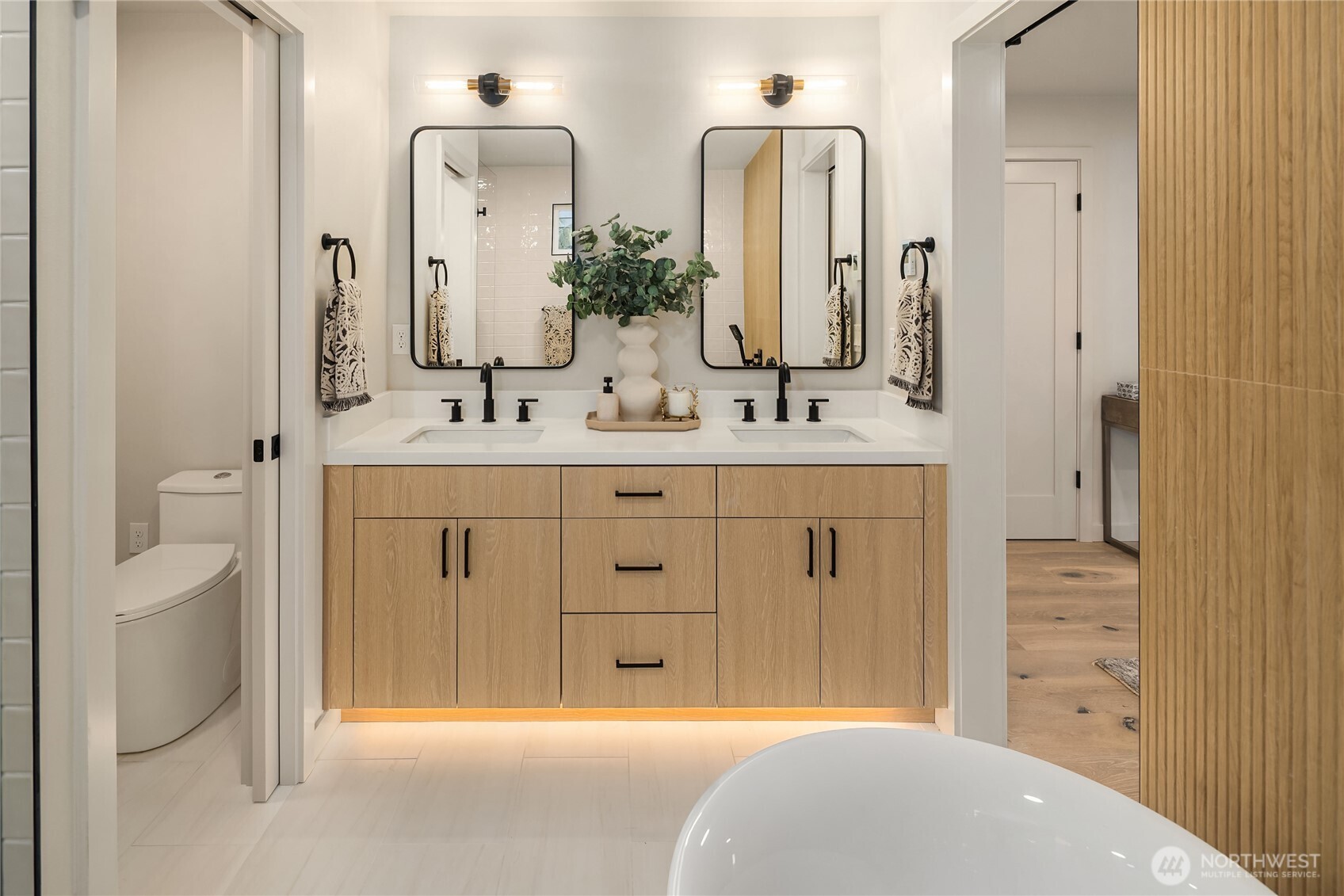 Bathroom with a double-sink oak vanity, black-framed mirrors, and a freestanding soaking tub.