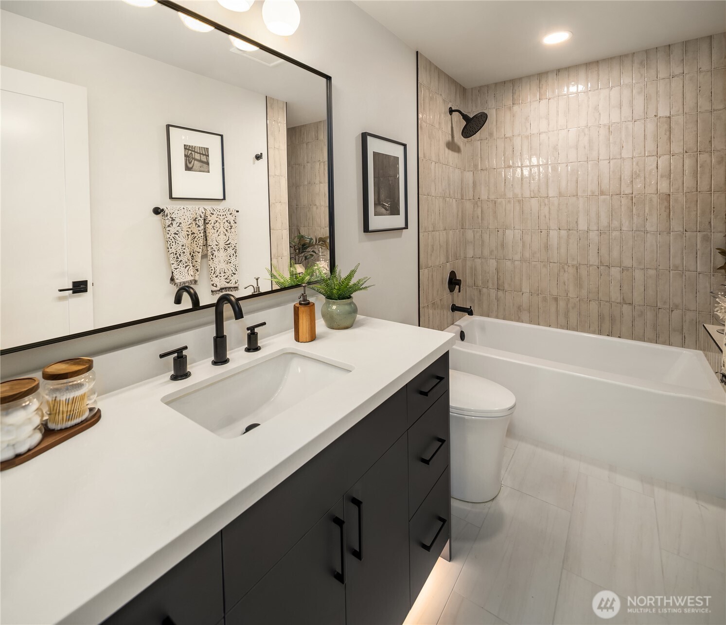 Bathroom with dark vanity, white countertop, and bathtub beneath beige tiled shower walls.