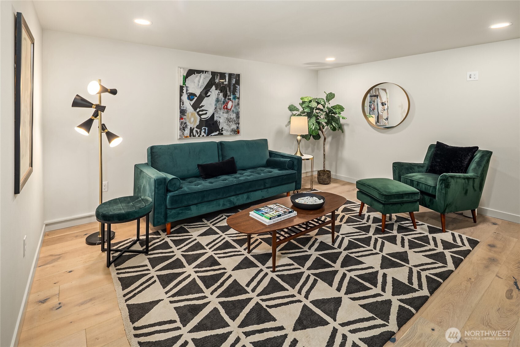 Staged living room with teal velvet seating, a geometric rug, and light hardwood floors.