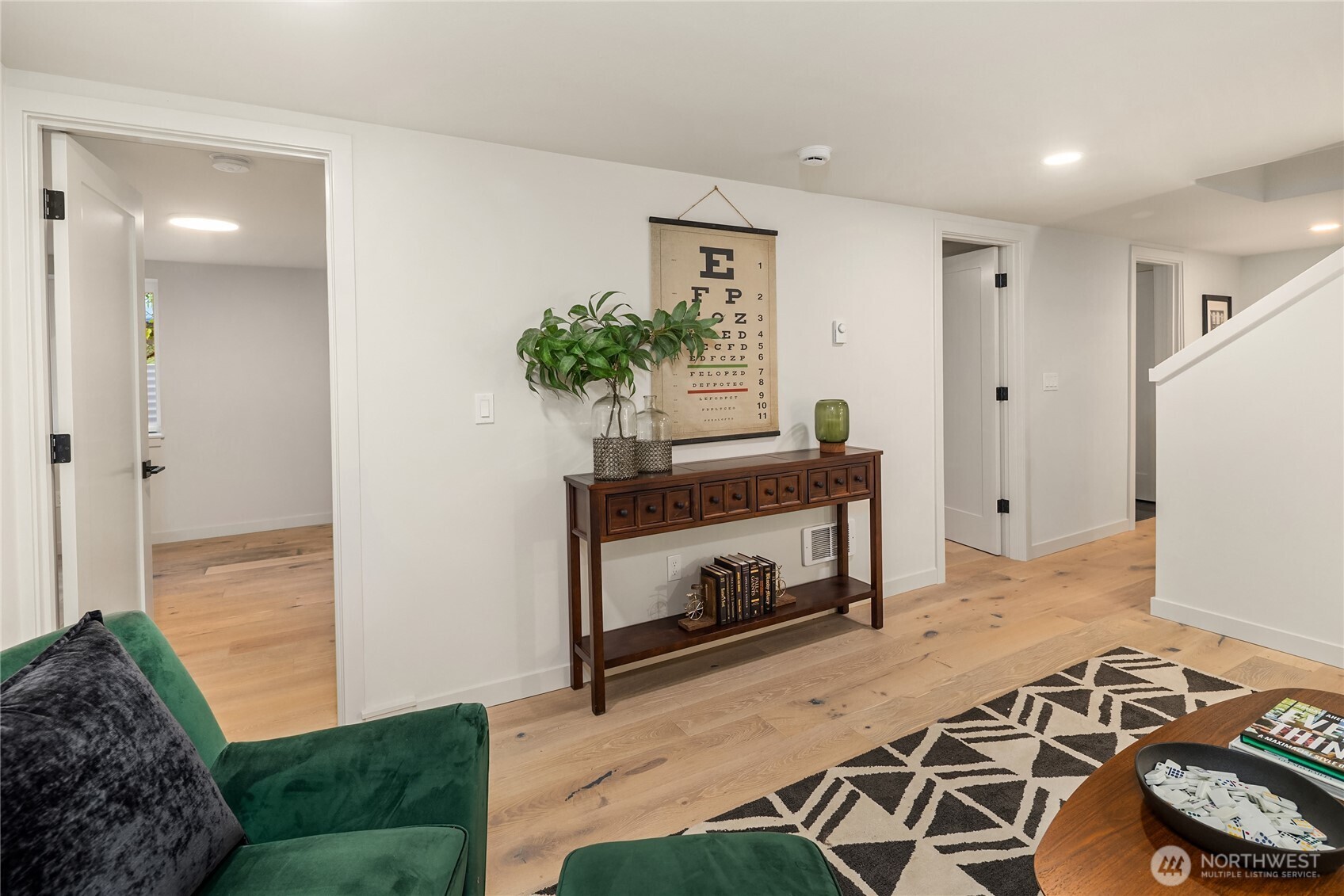 Furnished hallway with light oak floors, green velvet chair, wooden console table, and stairway.