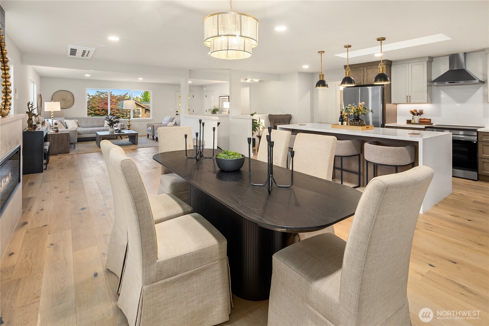 Open-plan dining room with a dark table, light upholstered chairs, and a white kitchen island.