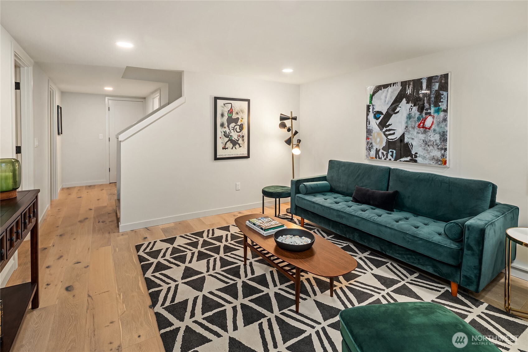Living room with a teal velvet sofa, geometric rug, and light oak floors.