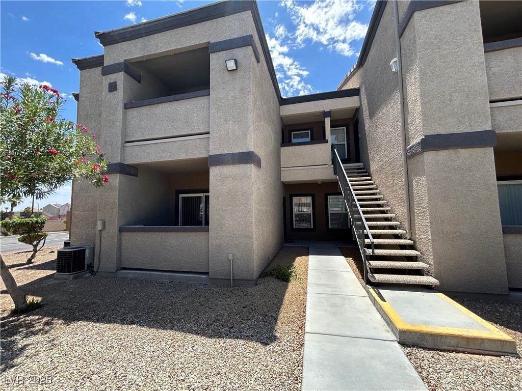 Two-story stucco condominium exterior with an outdoor staircase and gravel landscaping.