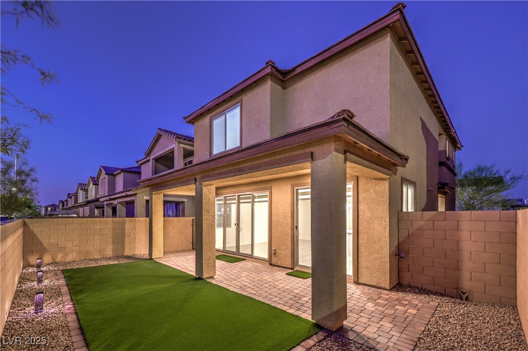 Two-story stucco home with a covered patio, artificial turf, and paver courtyard at dusk.