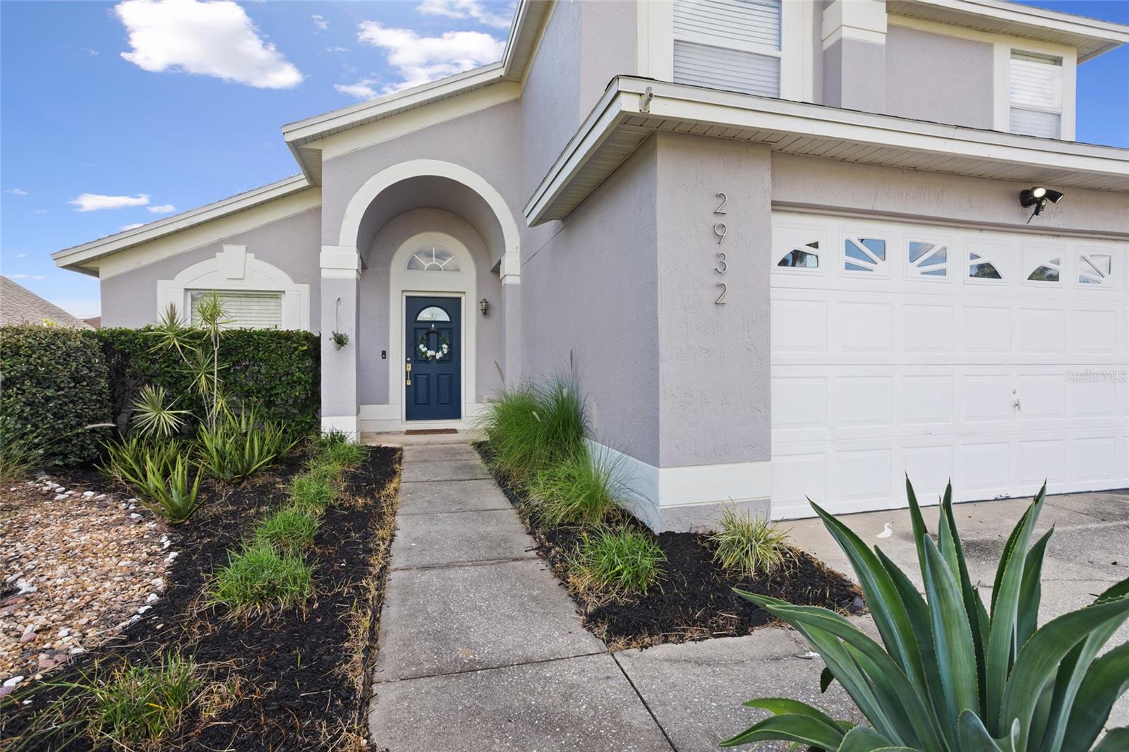 Lavender two-story home with a blue front door, arched entry, and white garage door.