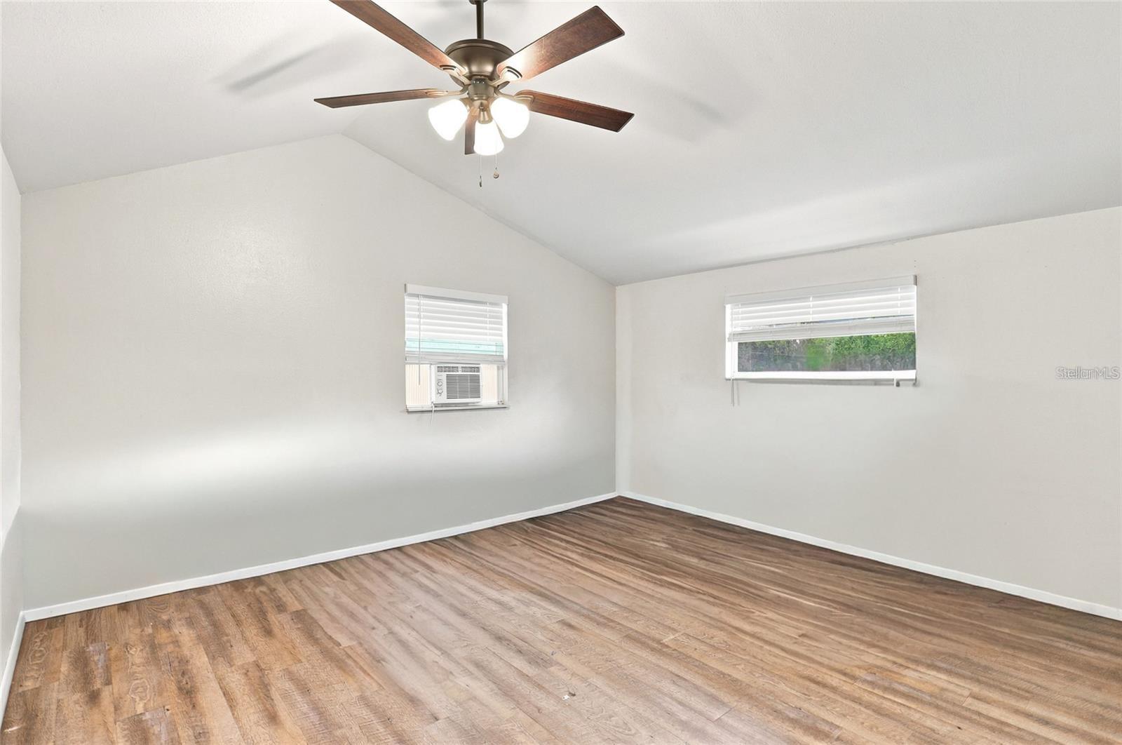 Empty bedroom with wood-look flooring, vaulted ceiling, ceiling fan, and window air conditioner.