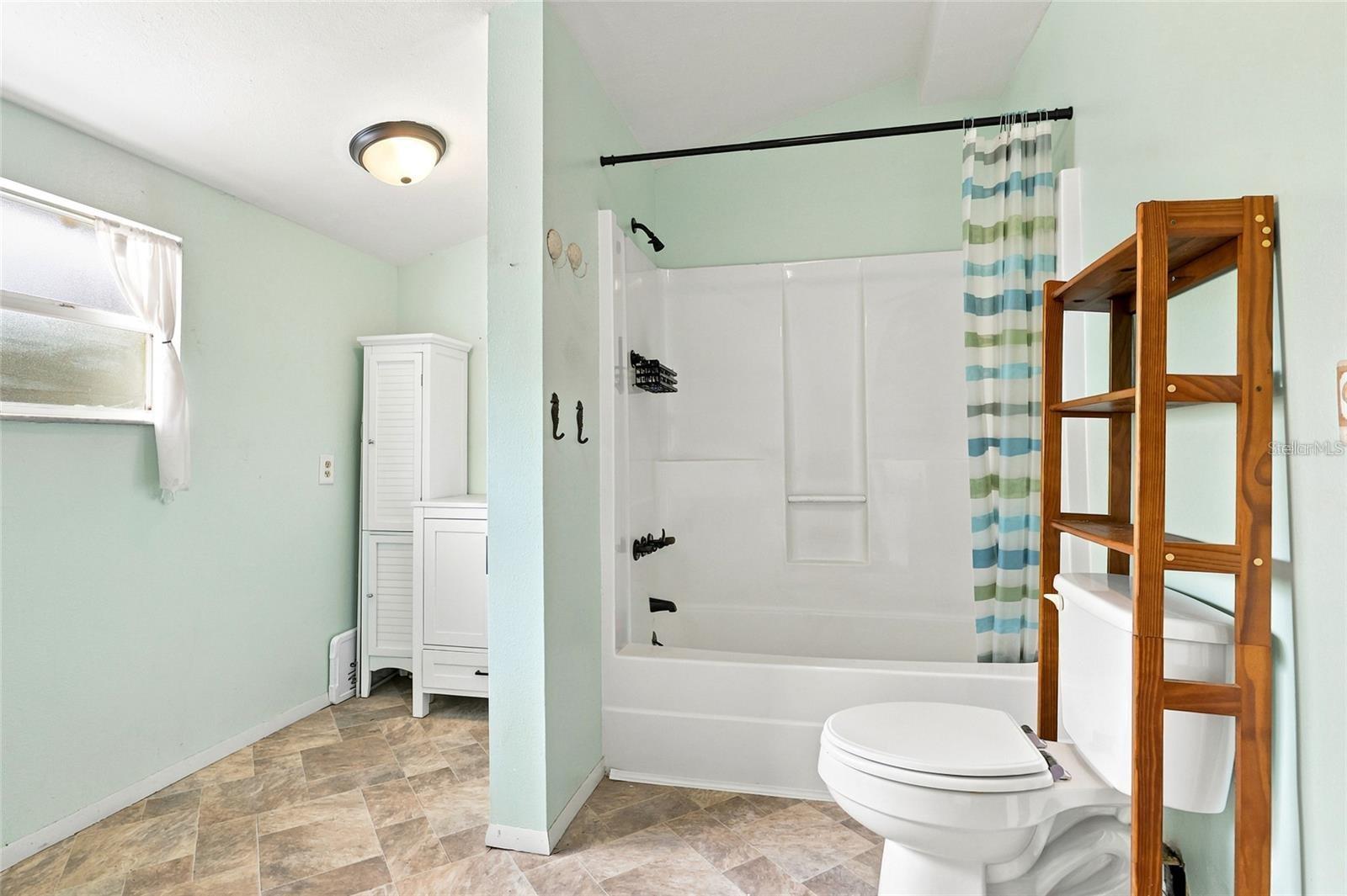 Bathroom with a white tub and striped shower curtain, mint-green walls, and wooden shelving.