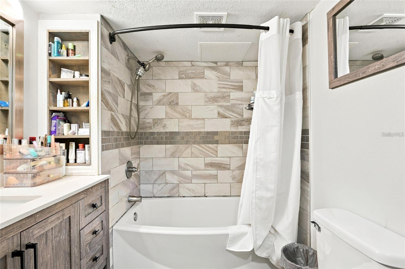 Bathroom with a tiled tub and shower, white curtain, and wood-look vanity.