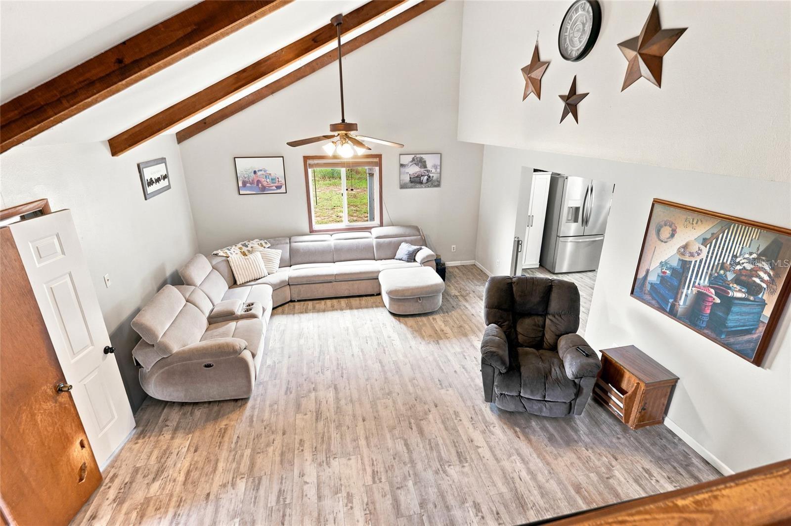 Living room with vaulted exposed-beam ceiling, gray sectional, ottoman, and adjoining kitchen.