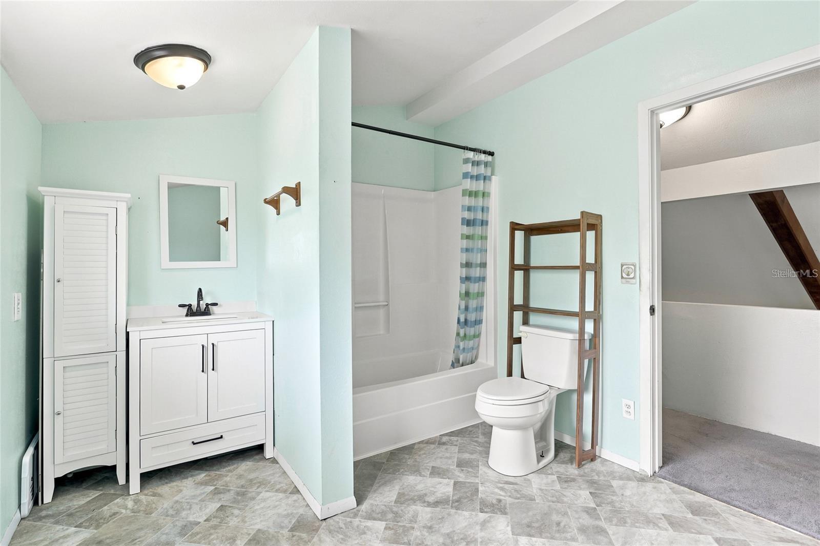 Bathroom with pale mint walls, gray tile floors, a white vanity, tub, and toilet beside wooden shelving.