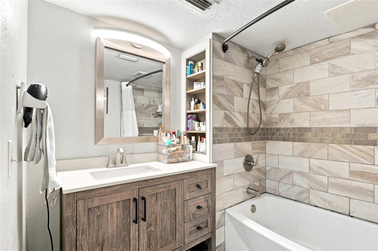 Bathroom with a wood-grain vanity and bathtub beneath a large tiled shower surround.