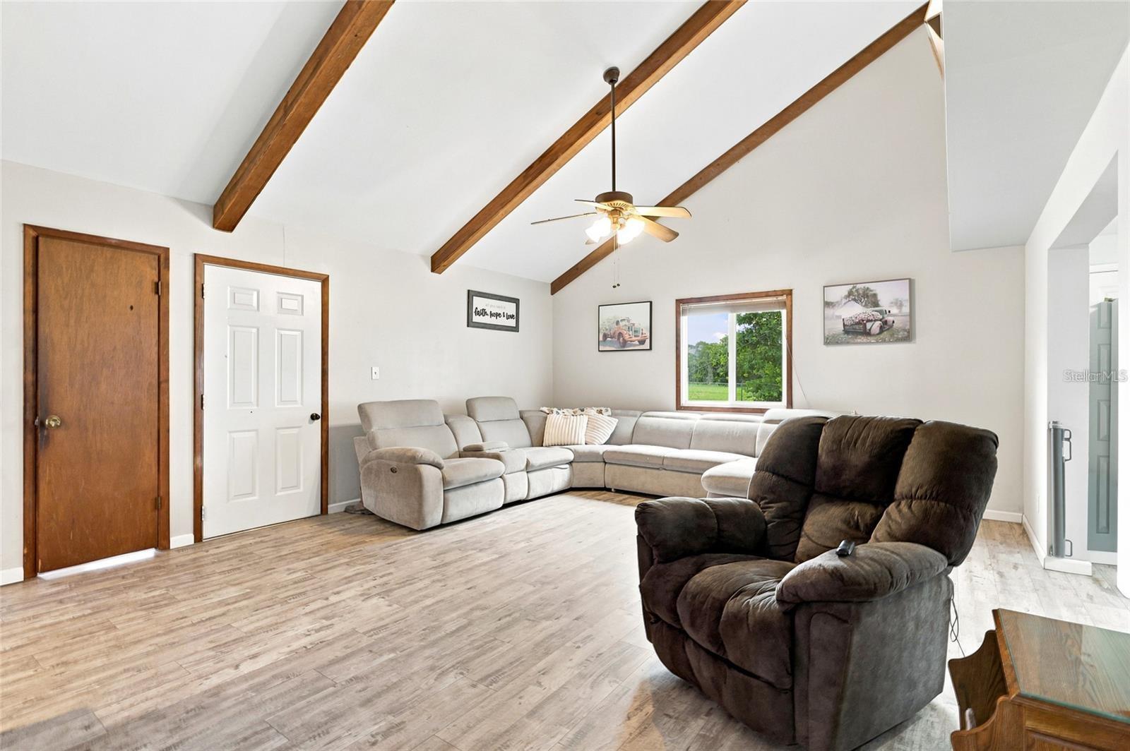Living room with exposed wood ceiling beams, a light sectional sofa, and dark recliners.