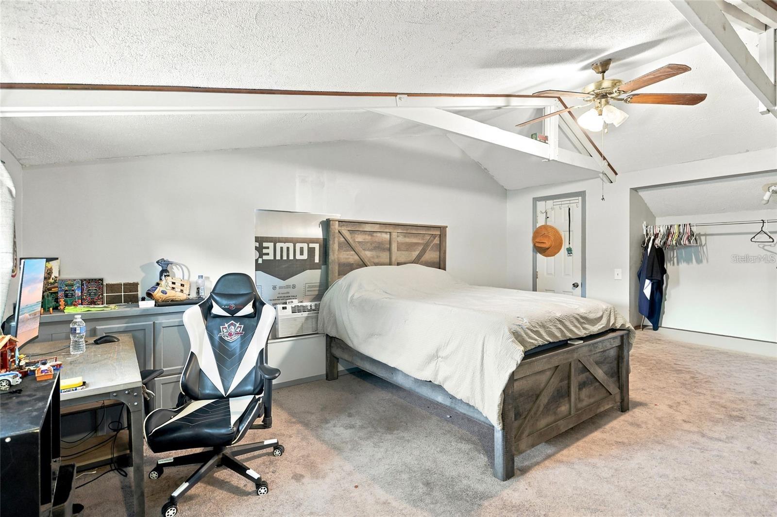 Bedroom with a dark wood bed, gaming chair, desk, and open clothes closet.