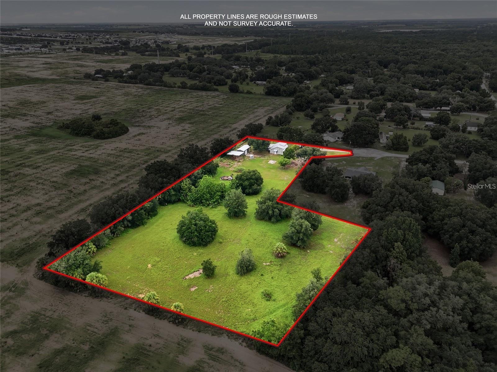 Aerial view of a grassy, tree-dotted property outlined in red, with a house and outbuildings near the road.